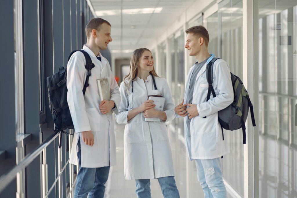 Three young medical professionals in lab coats talking in a hospital hallway.